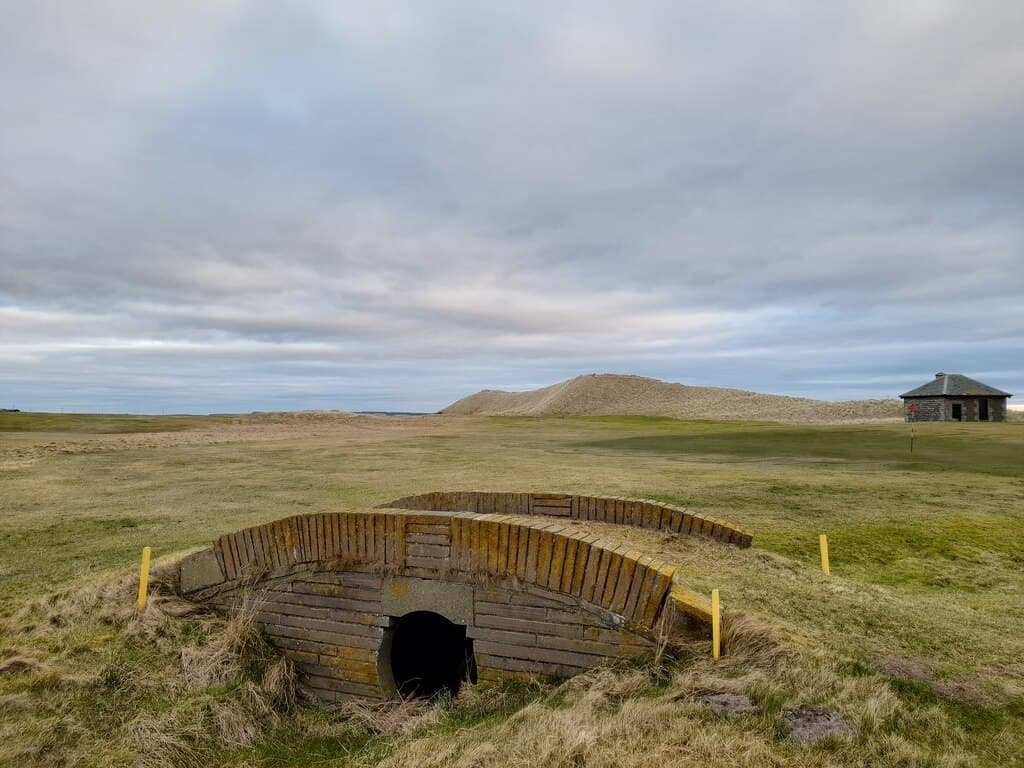 A stone bridge over a burn on the links at Wick, the dunes and a shelter beyond