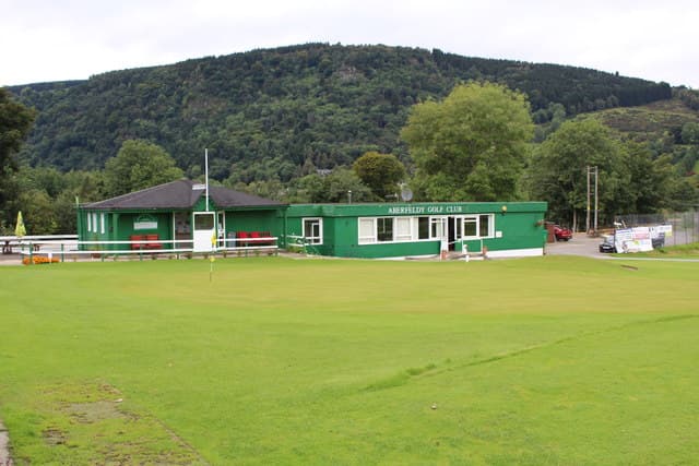 The green-painted clubhouse at Aberfeldy, wooded hills behind